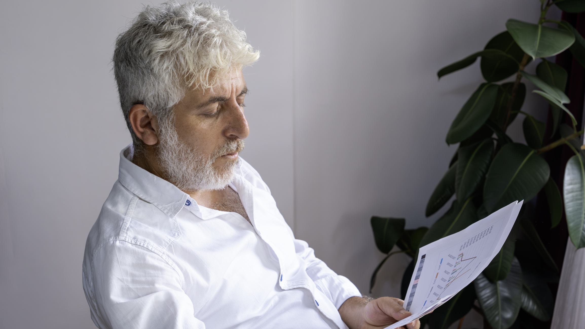 White Hair And White Beard Businessman Examines Company Profitability Reports